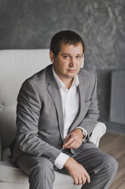 Gri patte kanepede oturan gri takım elbiseli bir genç adam