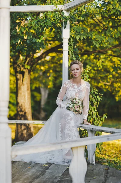 Νύφη με λευκό φόρεμα κάθεται σε ένα παγκάκι στο τον κήπο 247. — Φωτογραφία Αρχείου