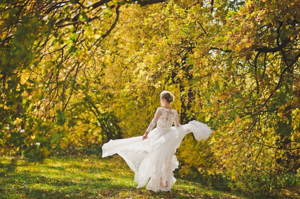 The bride happily spinning in the developing dress on the edge of the bright autumn forest.