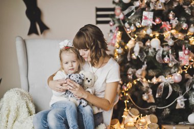 Anne ve kızı büyük bir saat önünde beyaz sandalyede 