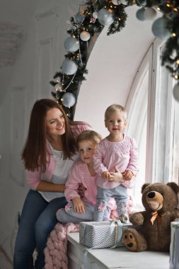 Pencerenin kenarında oturan iki küçük kızı olan bir anne.,