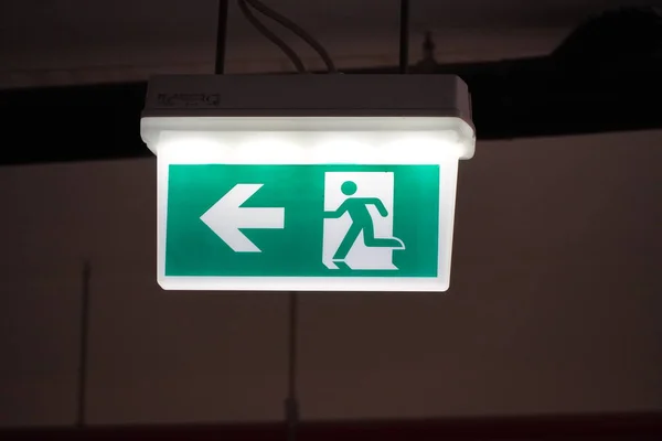 在建筑物中发出带有左箭头的紧急出口标志。安全第一的概念。复制太空壁纸。建筑物泊车处有灯光的出口标志. — 图库照片