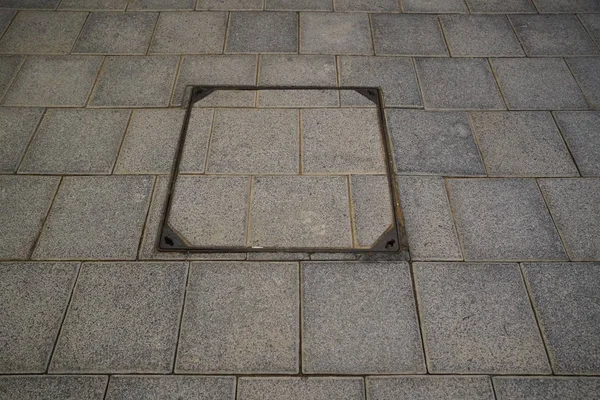 Tapa de alcantarilla cuadrada oculta, tapa de alcantarilla grunge. Cubierta de alcantarilla de hierro fundido en el antiguo camino peatonal de piedra adoquinada gris acera cuadrada pavimento en la ciudad. Vista superior, horizontal. — Foto de Stock