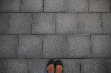 Kadınlar asfalt beton zeminde kare kiremitlerle durup dinlenen siyah ayakkabılar giyerler. Üst Manzara. Beton döşeme desenli asfalt. Ayakların ve Bacakların Selfie Kadını Yukardan Görüldü.