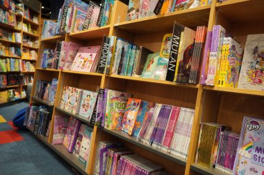 Satılık bir kitapçıda raflara kitap çizip boyayan çocuklar. Kütüphane çocukları kitapları bölümü. Kütüphane 'deki kitaplıkta satılık kitapların çeşitliliği. Süpermarket. Dubai Uae Aralık 2019.