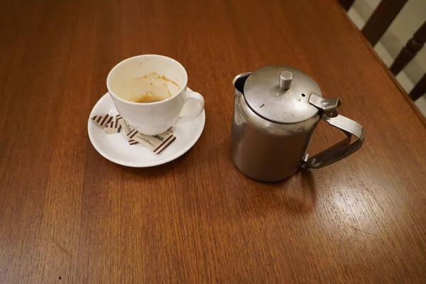 Alte schmutzige gebrauchte Aluminium-Teekanne Wasserkocher mit schmutzigem gebrauchten weißen Teebecher. Antiker Aluminiumkessel mit Teetasse und leeren gebrauchten Zuckerbeuteln. Schmutzige Kaffee- und Teetasse halb leer auf Untertasse auf Tisch. — Stockfoto