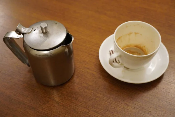 Tetera de aluminio usada sucia vieja con taza de té blanca usada sucia. Hervidor de aluminio antiguo con taza de té y sobres de azúcar usados vacíos. Café sucio y taza de té medio vacío en platillo en la mesa. —  Fotos de Stock