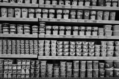 Dükkandaki rafta bulunan yoğurt çeşitliliğinin siyah ve beyaz görüntüsü. Yunan, sade, aromalı, meyveli yoğurt. Farklı marka yiyecek ve içeceklerle satılan büyük buzdolabının iç manzarası. Dubai BAE Aralık 2019