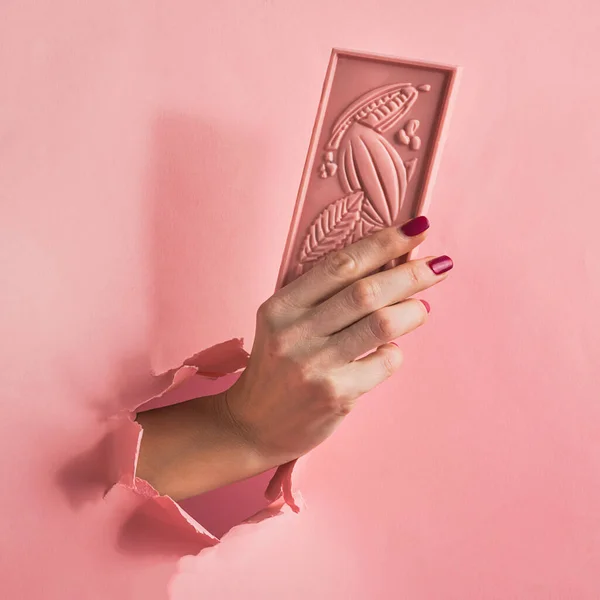 Çikolata pembesi bir kadın elini pembe bir arka plan kağıdında tutuyor. Yemek sanatı. Kare kare