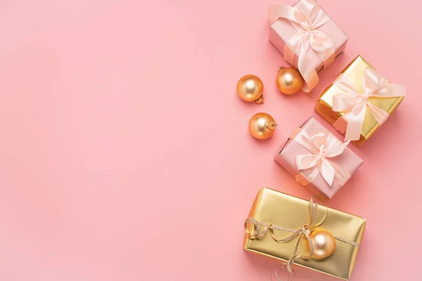 Scatole festive con fiocco nastro di raso palle giocattolo d'oro uno sfondo rosa pastello. Struttura piatta. Concetto vacanza. Copia spazio . — Foto Stock