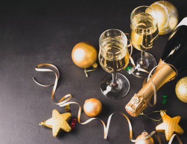 Siyah arka planda iki bardak şampanya şişesi altın noel oyuncakları yılanbalığı yıldız topları. Yeni yıl konsepti.