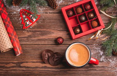 Çikolata şekerlemeleri kırmızı el sanatları kutusundaki sıcak içecekler ahşap bir Noel arka planında Yeni Yıl oyuncağının köknar dalları.