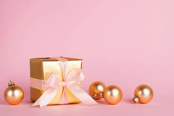 Праздничная коробка с атласным луком и золотыми игрушечными шариками на розовом фоне. Концепция праздника. Копирование пространства — стоковое фото
