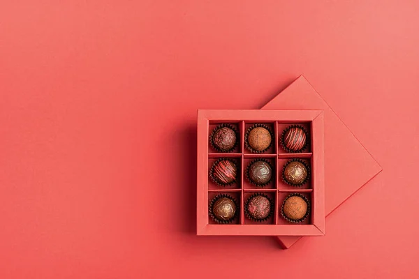 Шоколадные конфеты в красной коробке ремесла на ярком коралловом фоне. Плоская планировка. Праздник — стоковое фото