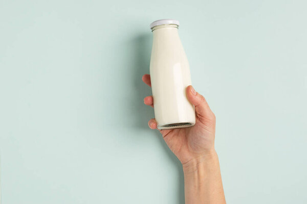 Female hand holds milk or white milk drink in a glass bottle on white background. Healthy eating concept. Flat layout .