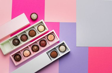 Renkli kağıt arka planda pembe mavi kutularda çeşitli çikolatalar. Düz bir manzara. Uzayı kopyala Tatil