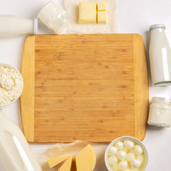 Dairy and sour-milk fermented organic products are laid out in a frame near cutting wooden board on a white background.