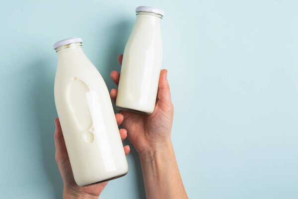 Female hand holds two bottles of sour milk product blue pastel background. The concept healthy diet diet. Flat top view.