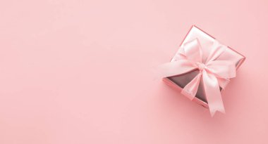 Altın ambalajlı, pastel pembe arka planda saten fiyonklu bir kutuda. Düz stil yerleşimi. Tatil kavramı.
