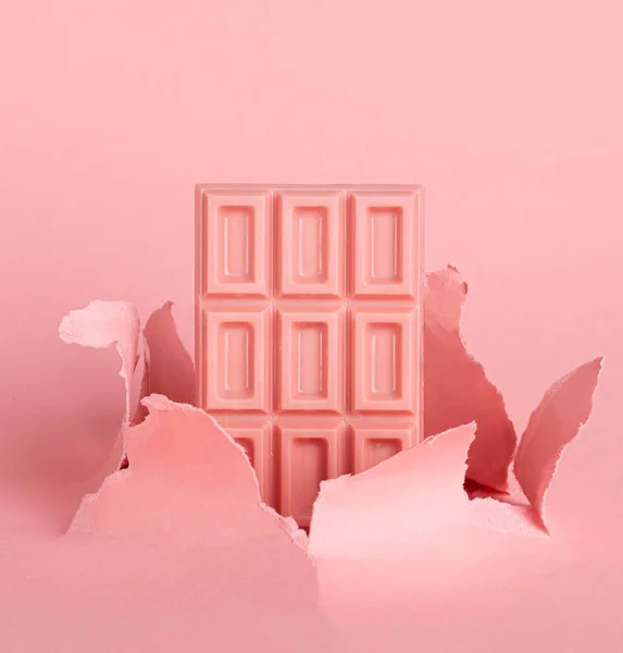 Telhas de chocolate rosa no fundo pastel contra o fundo de papel de explosão buraco. O conceito de comida é minimalismo . — Fotografia de Stock