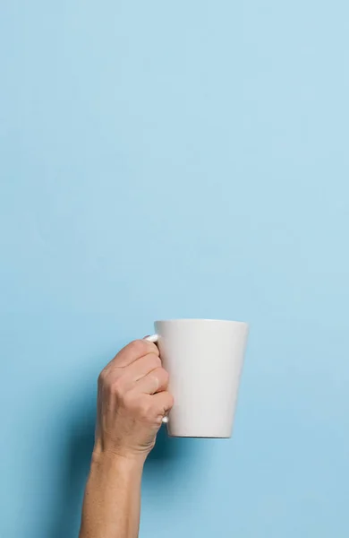 Woman holds in her hands a cup of coffee or tea drink blue bright background. Food drink concept. Copy space.