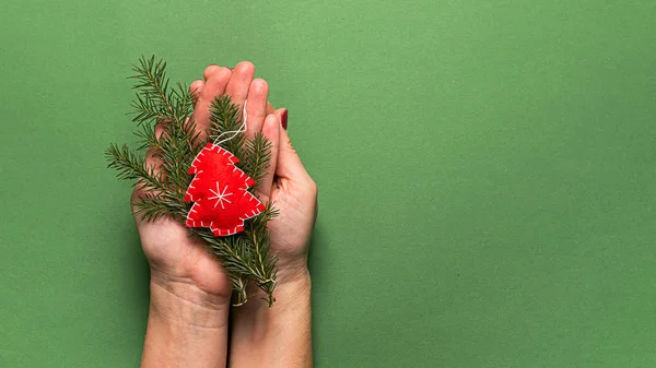 Weihnachtsbaumspielzeug aus Naturmaterialien und Tannenzweigen in Frauenhand, Hände auf grünem Hintergrund. — Stockfoto