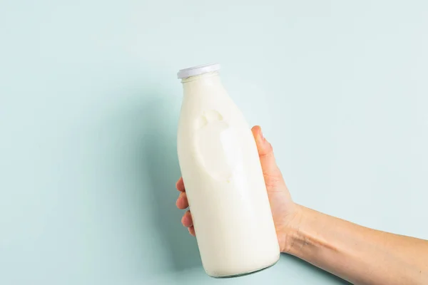 Ženská ruka drží mléko nebo bílý mléčný nápoj ve skleněné láhvi na bílém pozadí. Zdravý stravovací koncept. Ploché uspořádání . — Stock fotografie