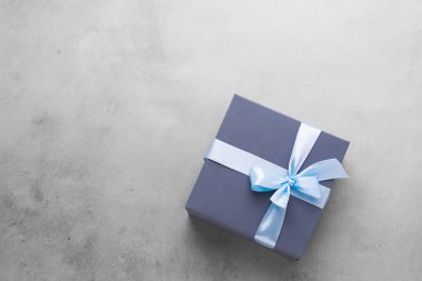 Beton gri arka planda saten fiyonklu şenlikli mavi hediye. Düzen düz stil. Tatil konsepti. Boşluğu kopyala