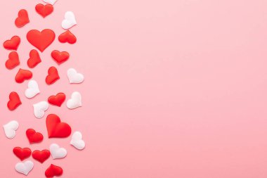 Pembe arka plana dağılmış aşkın kırmızı ve beyaz kalpleri. Sevgililer Günü konsepti. Yatay çerçeve kopyalama alanı.