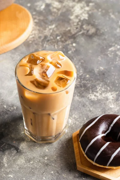 Iced black coffee with ice cubes tall glass and a fresh chocolate donut. Refreshing drink on the table gray background.