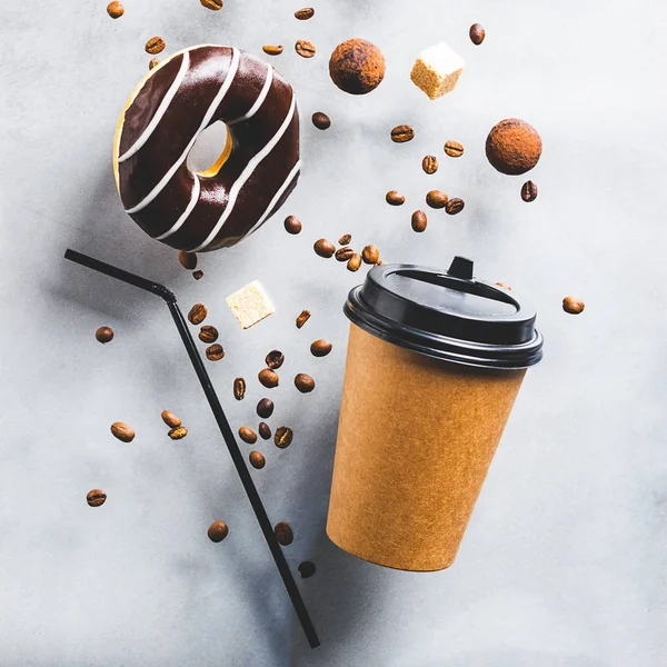 Paper cup with coffee drink or tea donut in chocolate coffee beans on a gray background. Creative fashionable levitation