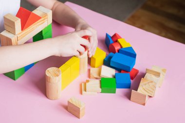 The child collects the designer builds a house of wooden cubes. Toys from environmental natural materials for children.