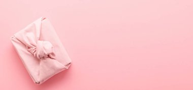 Pembe arka planda Furoshiki tarzında kumaşa sarılı tatil hediyesi. Sıfır Atık Yaşam Tatili Konsepti.
