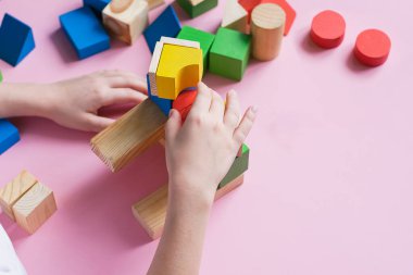 The child collects the designer builds a house of wooden cubes. Toys from environmental natural materials for children.