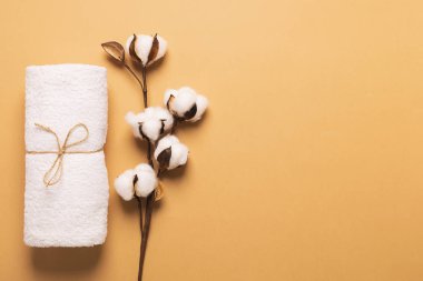 A clean white soft towel is rolled up and tied with a canvas rope with a cotton branch on a brown background. Zero West.