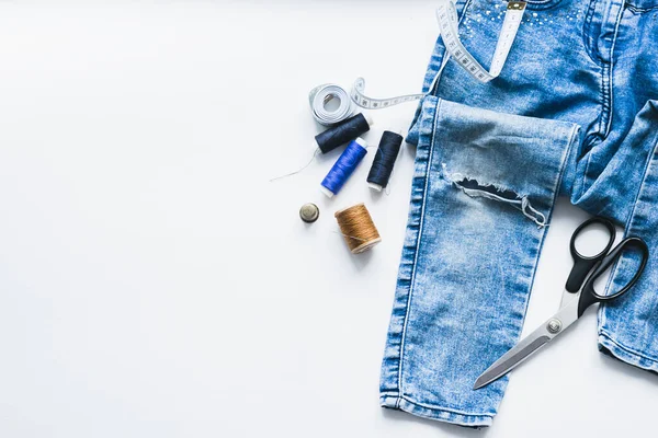 Handicraft, clothing repair. Ripped blue jeans sewing accessories white background. The concept of economical things. — Stock Photo, Image