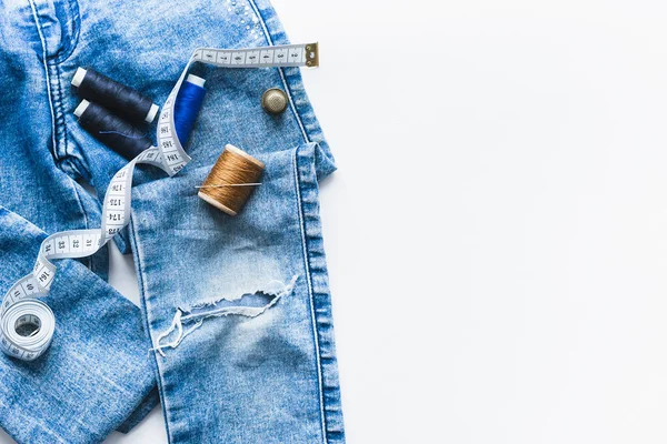 Hantverk, reparation av kläder. Rippade blå jeans sy tillbehör vit bakgrund. Begreppet ekonomiska saker. — Stockfoto