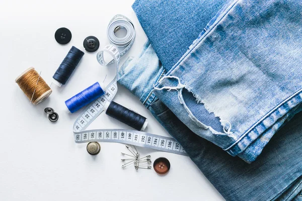 Handicraft, clothing repair. Ripped blue jeans sewing accessories white background. The concept of economical things.