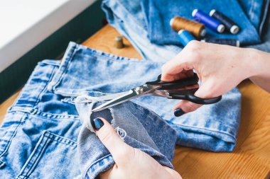 Bir kadın yırtık kot pantolonları tamir ediyor. Ekonomik yeniden kullanım kavramı. Ev yapımı dikiş..