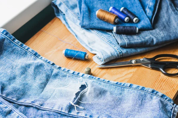 Handicraft, clothing repair. Ripped blue jeans lie on a wooden table. The concept of economical reuse of things.