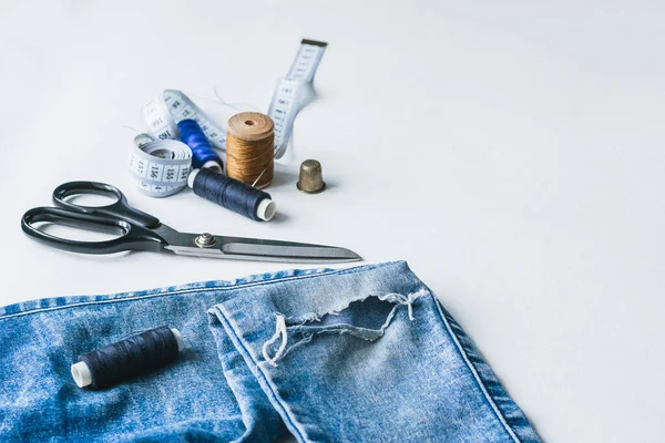 Handicraft, clothing repair. Ripped blue jeans sewing accessories white background. The concept of economical things.