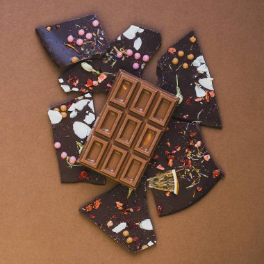 Meyve fıstığı ve dilimlenmiş kahverengi arka planla süslenmiş koyu sütlü çikolata. Minimalizm tek renklidir..