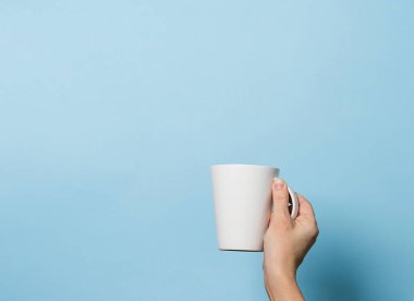 Kadın elinde bir fincan kahve ya da çay ile mavi parlak arka plan içer. Yiyecek içecek konsepti. Boşluğu kopyala.