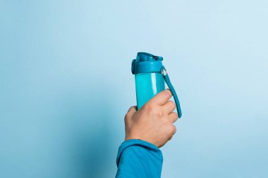 Bir adam mavi arka planda elinde bir su şişesi tutuyor. Spor içeceği konsepti. Metnin için boşluk kopyala
