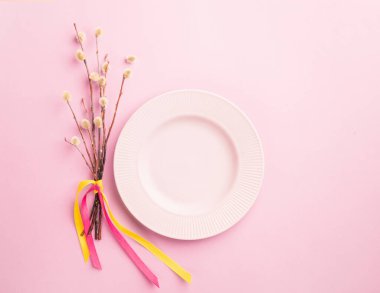 Empty plate of pussy-willow twig festive tied with a satin ribbon with a bow on a pastel pink background.