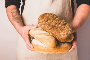 Önlüklü bir adam elinde altın gevreğiyle taze ekmek tutuyor. Ev yapımı fırın pişirme konsepti.