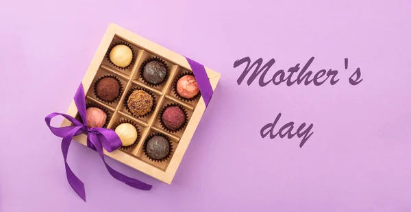 Set of different chocolates in a paper box with a satin ribbon on a bright background inscription Mothers Day. — Stock Photo, Image