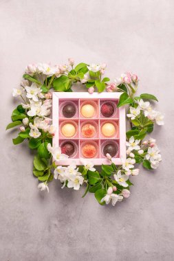 Çeşitli renkte çikolatalar, zarif bir kutunun içinde. Gri arka planda taze çiçeklerin süslendiği bir kutuda..