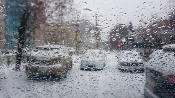Şehir ve arabaların arka planındaki arabanın camına yağmur damlaları ve karla karışık yağmur yağar.