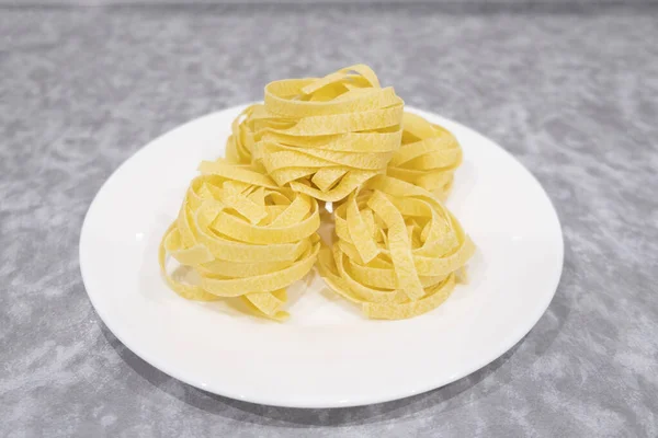 Many Italian egg pasta nest on a white plate on a gray background — Stock Photo, Image